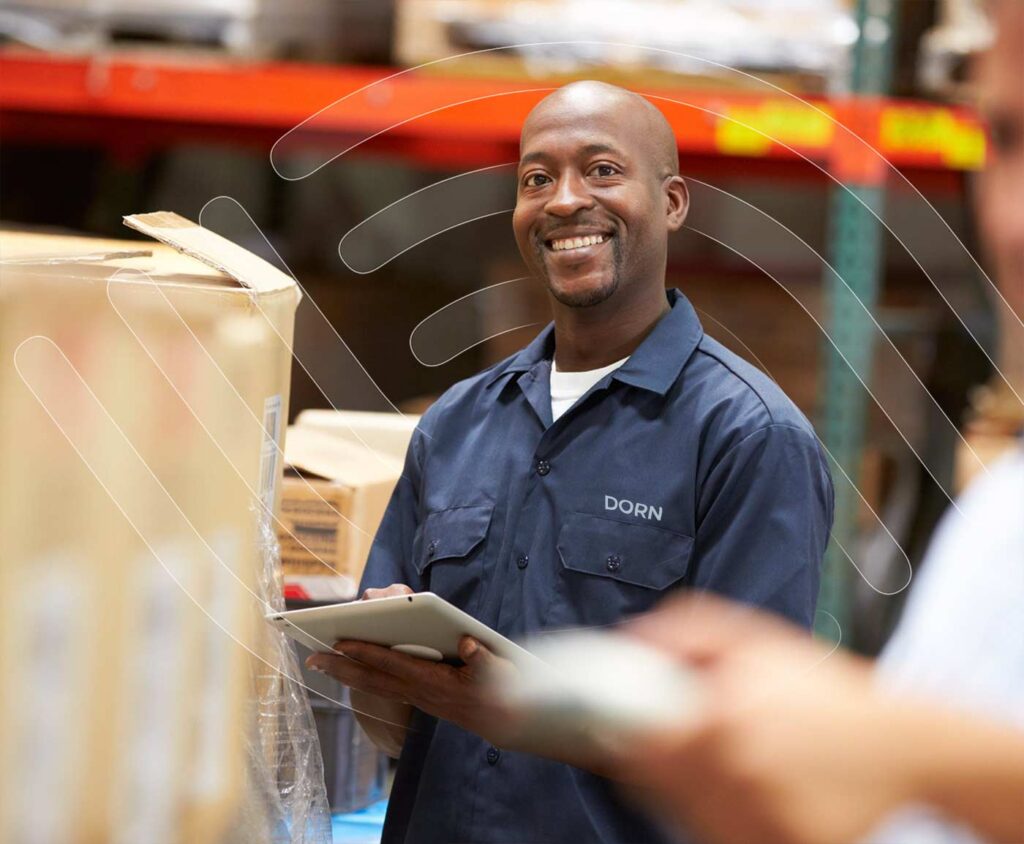 DORN employee smiling in a warehouse while holding a tablet, supporting a worker’s return to work program